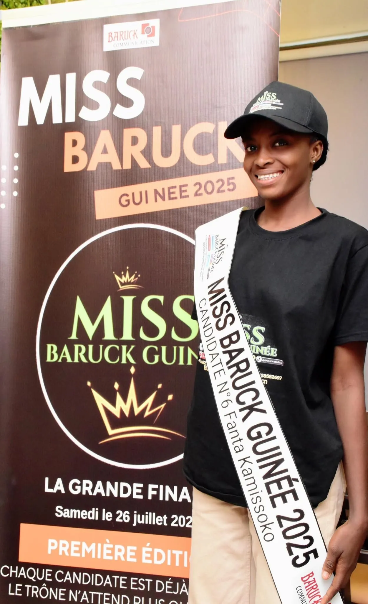 Une candidate devant l’affiche de la grande finale, tee-shirt et casquette Baruck