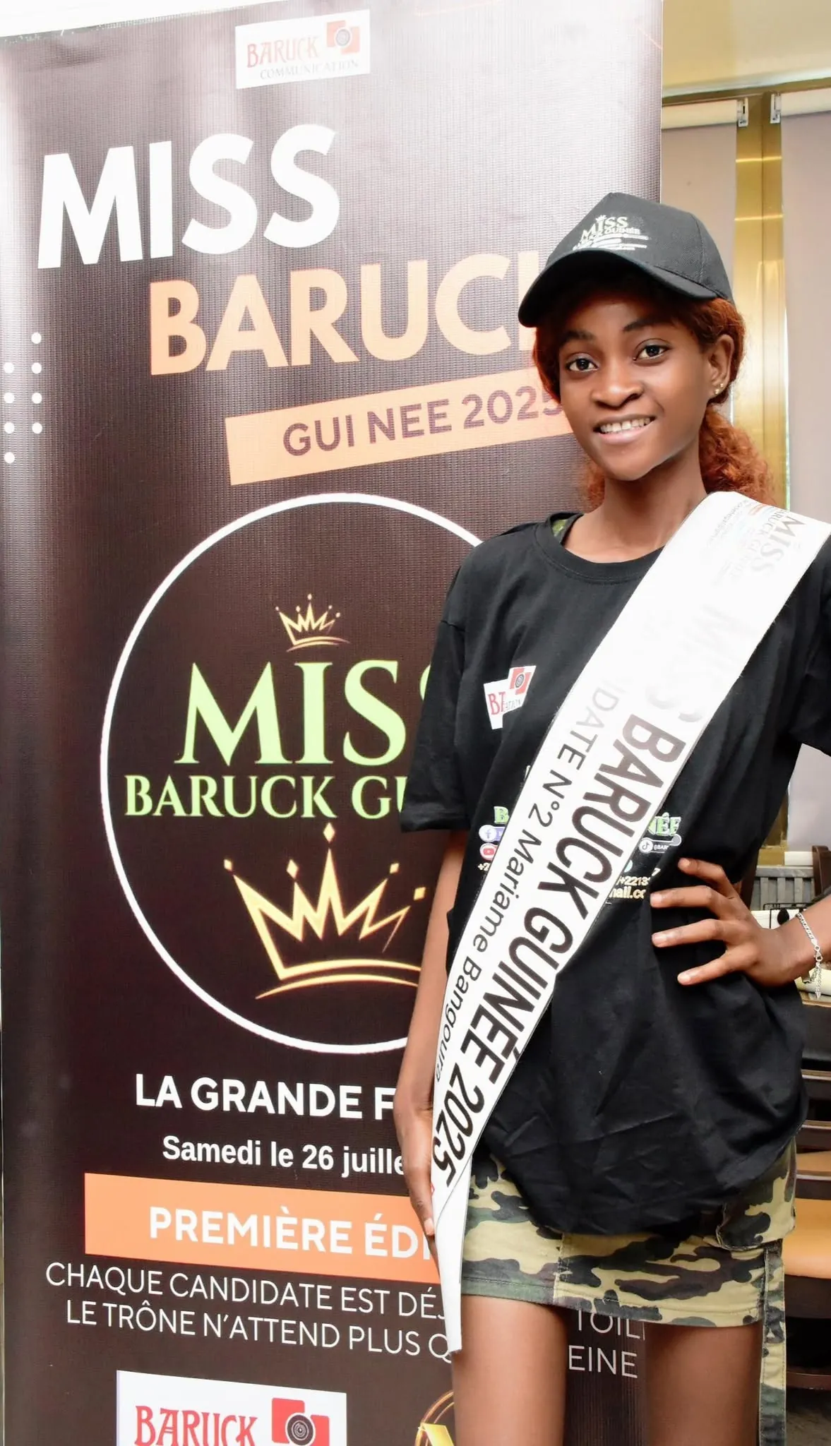 Une candidate posant devant l’affiche de Miss Baruck Guinée 2025