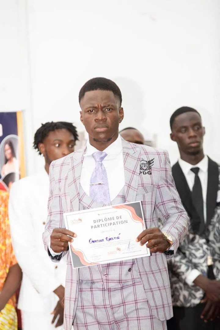 Un candidat présentant son diplôme de participation, en costume à carreaux